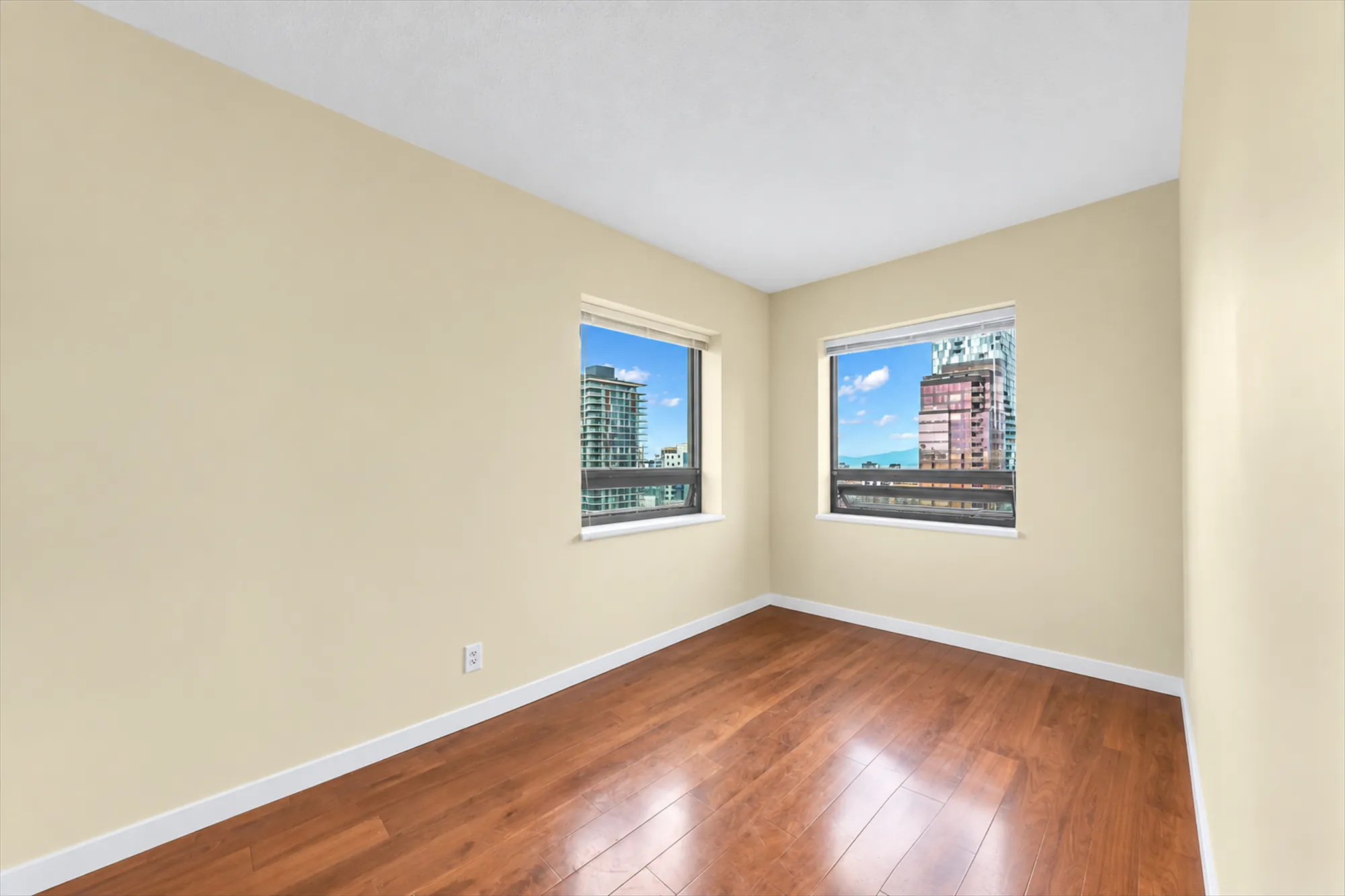 The small bedroom, empty: a window on each of two walls, cream walls, hardwood floors