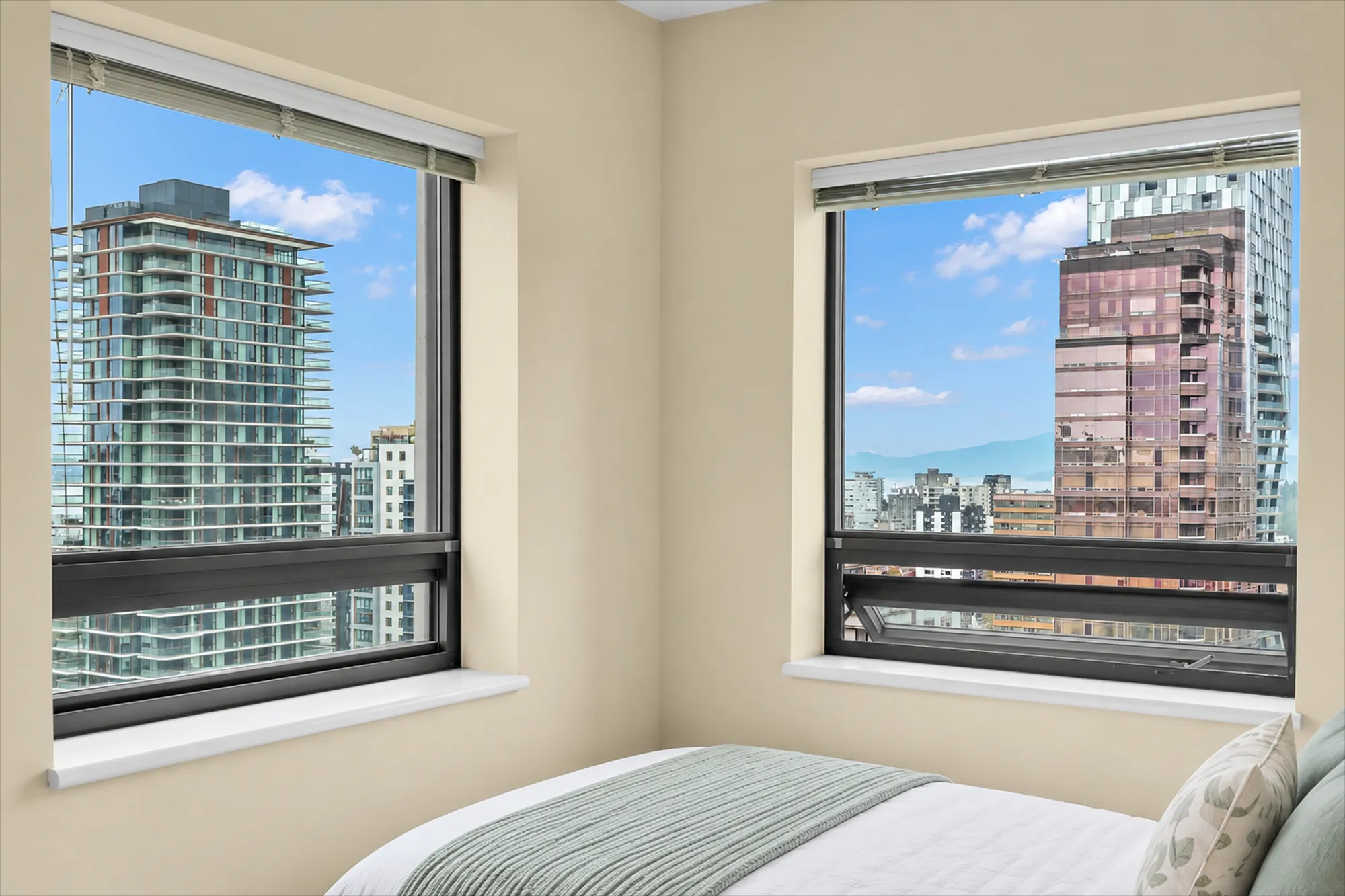The same view virtually staged: the foot of a bed with a green throw in the corner below the windows