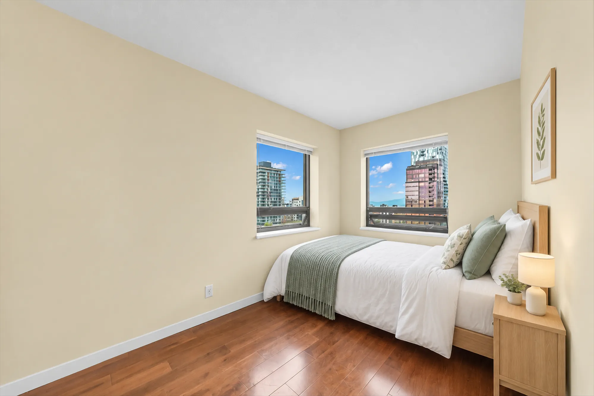 The same frame virtually staged: a bed with white bedding and a green throw, a wood night table and a lamp, a framed botanical print