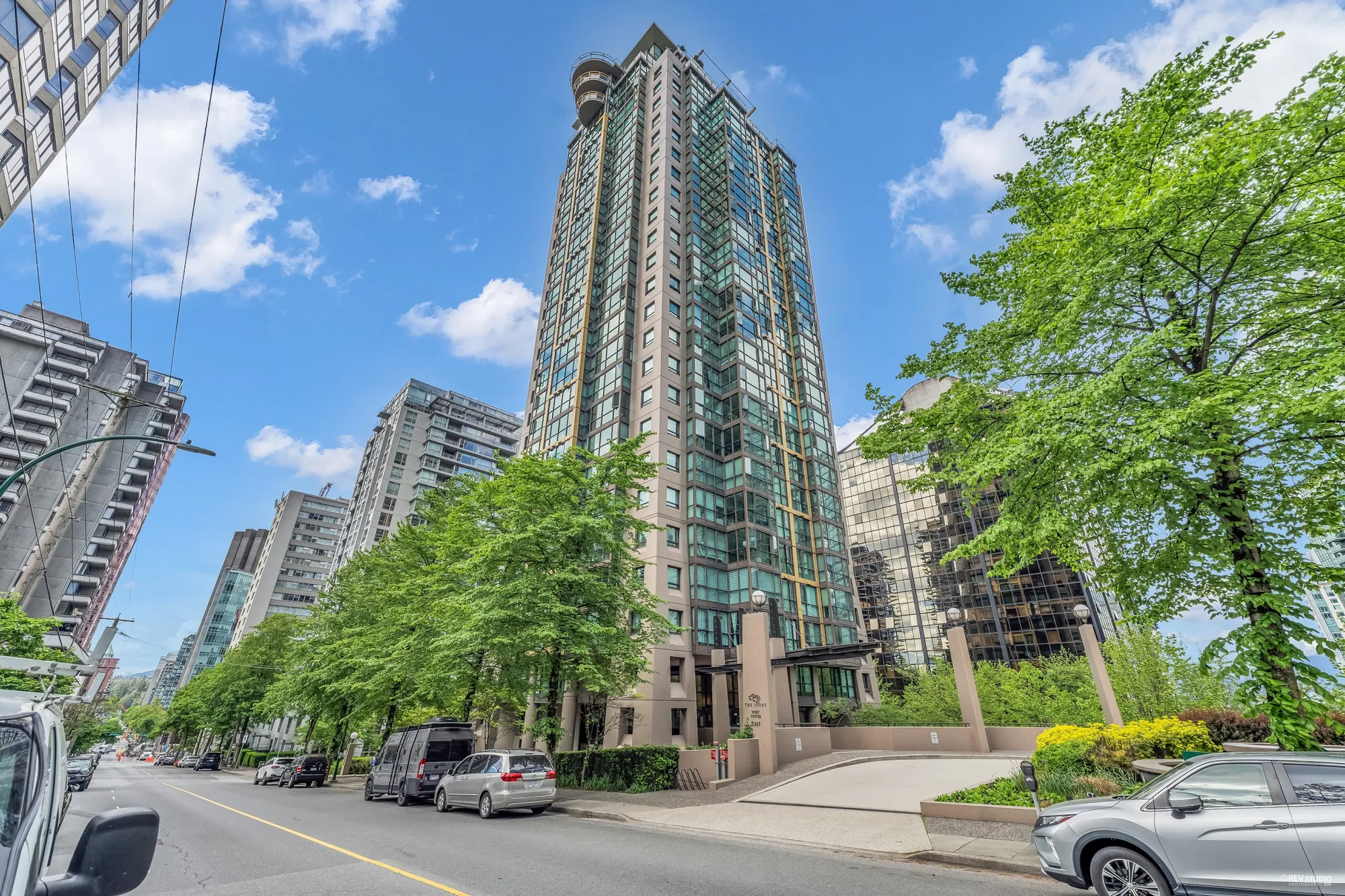 The Lions from the street: two glass and concrete towers among trees, cars along the curb