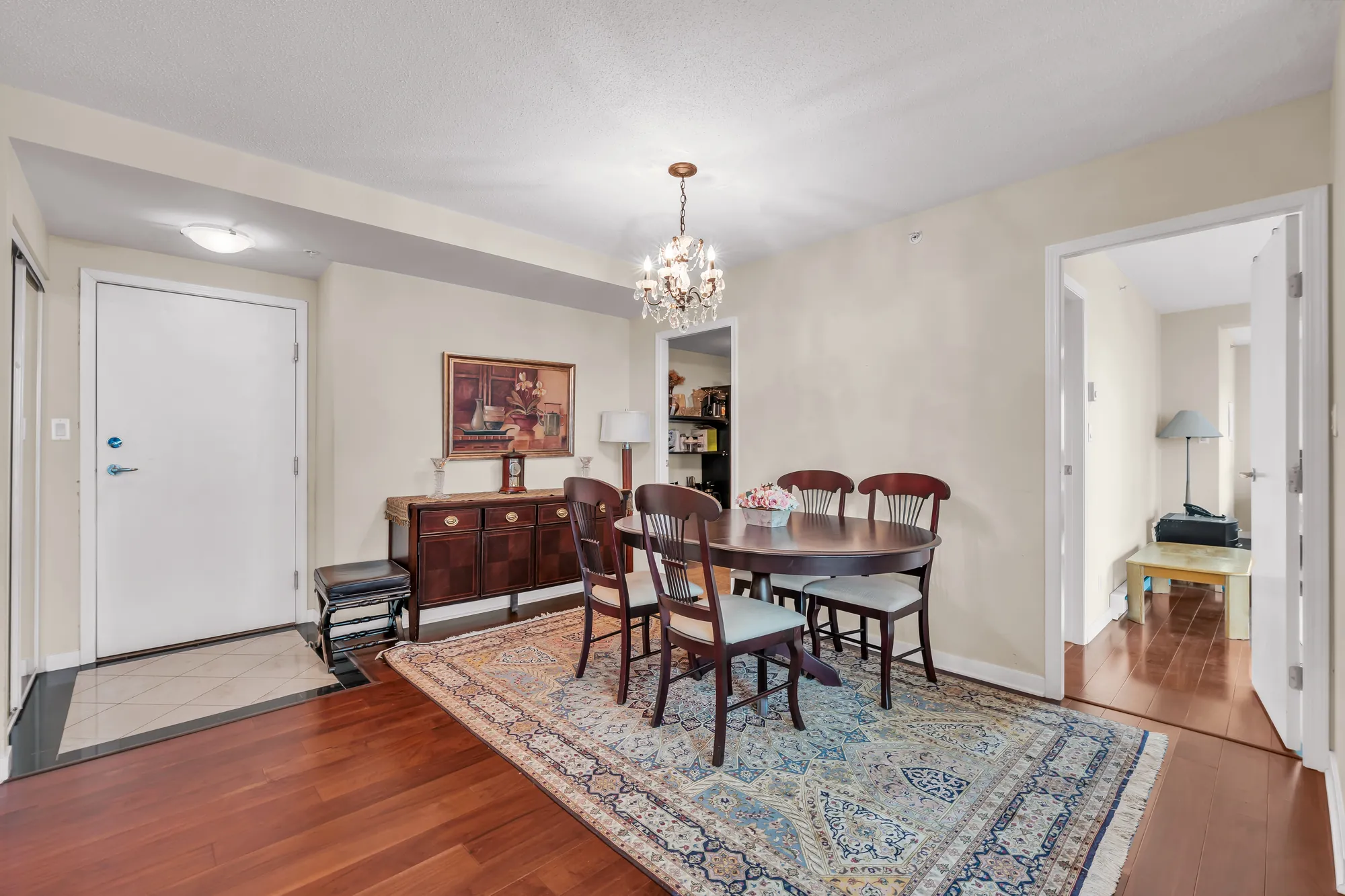The dining room: an oval table and chairs on a rug, a crystal chandelier, a sideboard, the front door at the left