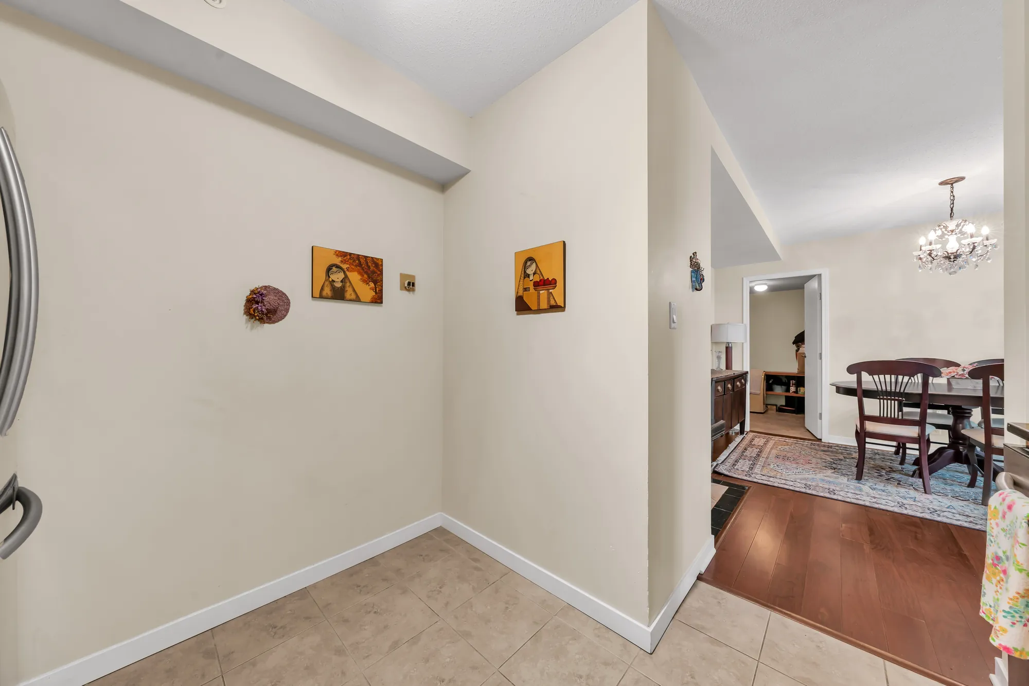 The foyer: a tiled floor and cream walls, two small paintings, the dining room and its chandelier through the opening at the right