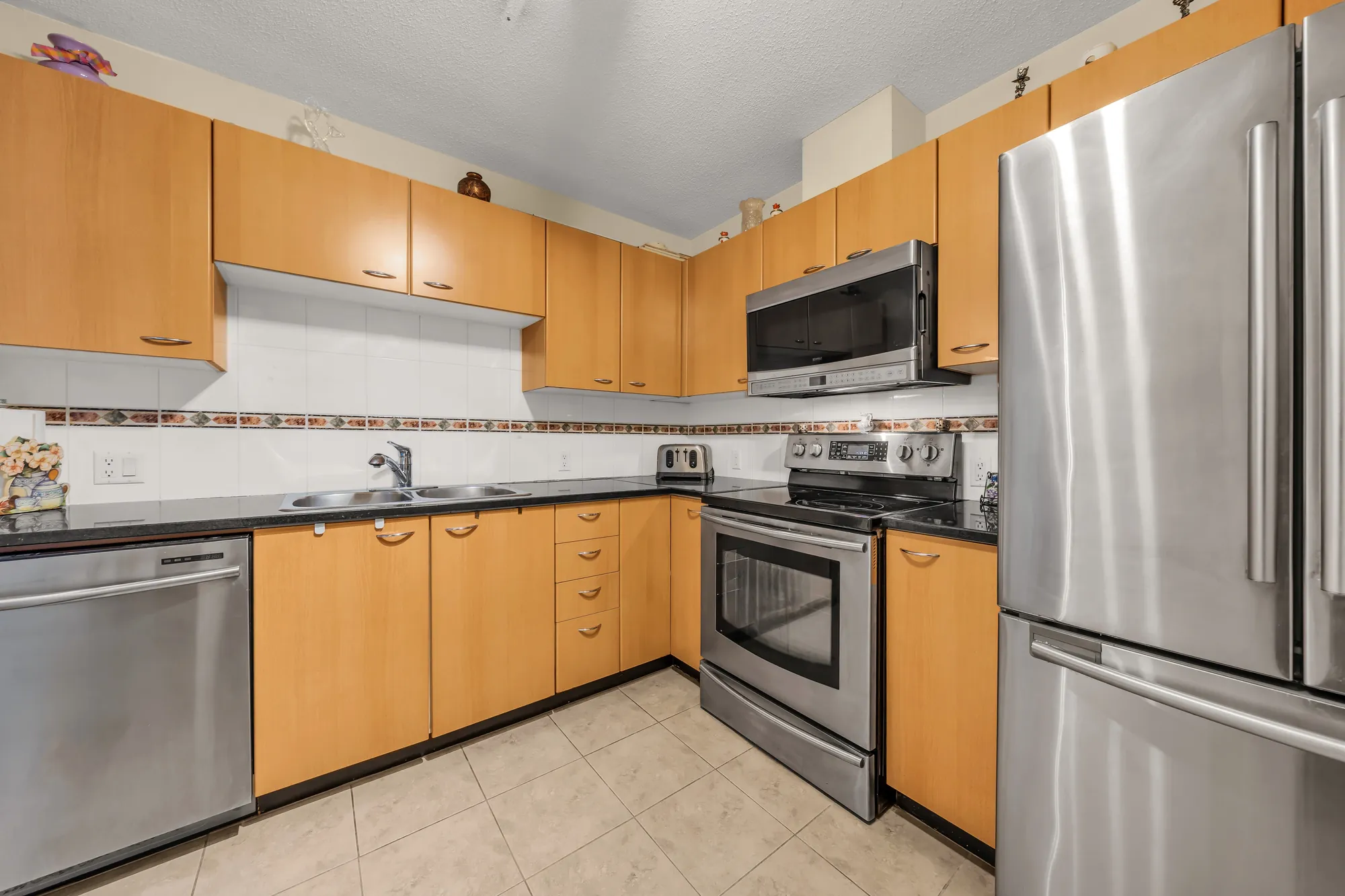 The kitchen from the doorway: maple cabinets, a stainless dishwasher, range, microwave and fridge