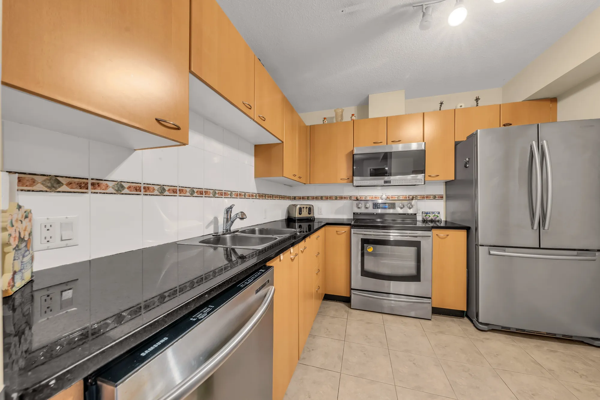 The sink wall: a double sink, black counters, maple cabinets above and below, the range and the fridge beyond