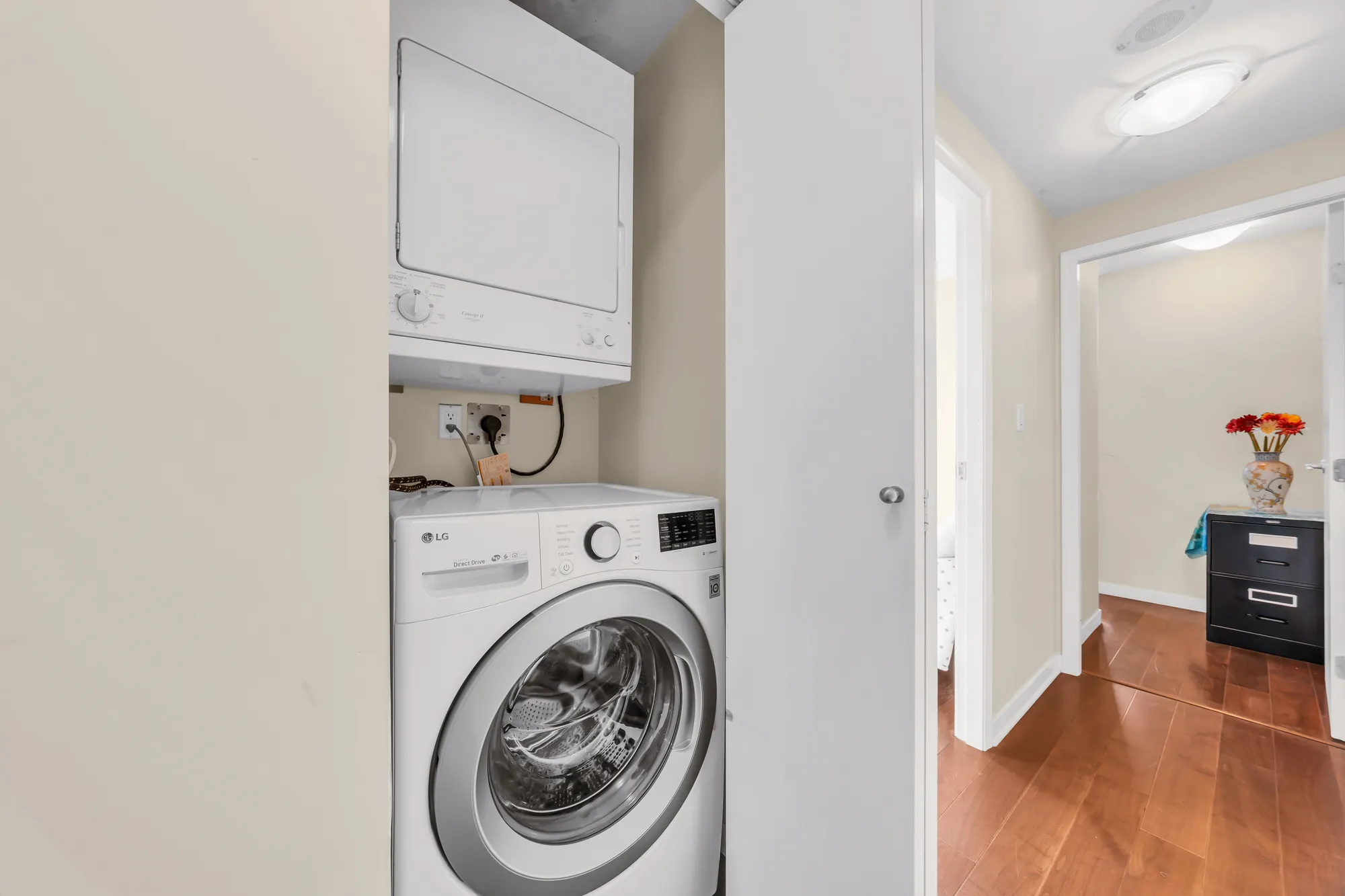 A stacked washer and dryer in a closet, the hall beyond to a bedroom