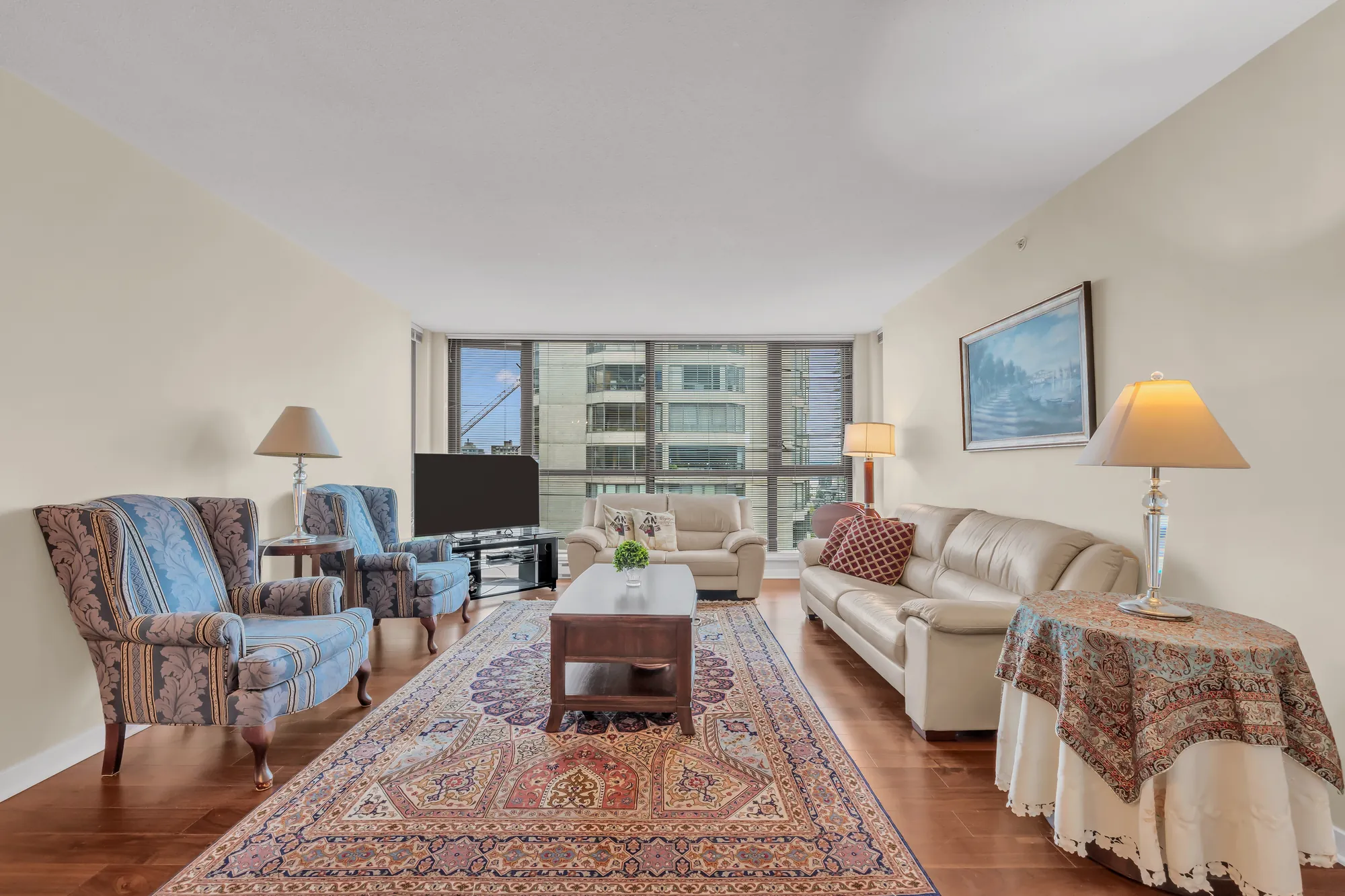 The living room toward the windows: patterned armchairs, the coffee table, a cream sofa and a table lamp