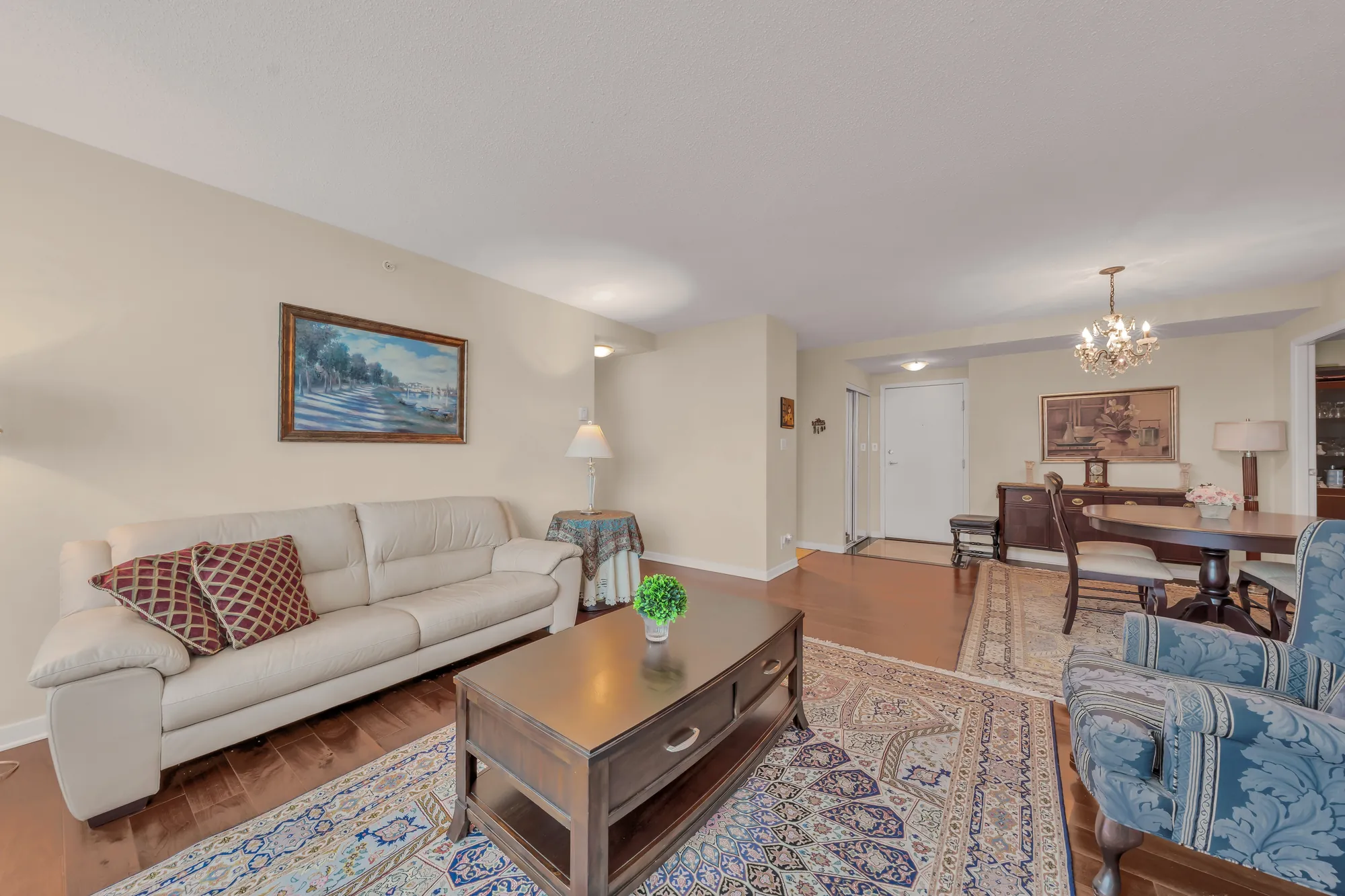 A cream leather sofa under a framed painting, the coffee table, the dining area and its chandelier beyond