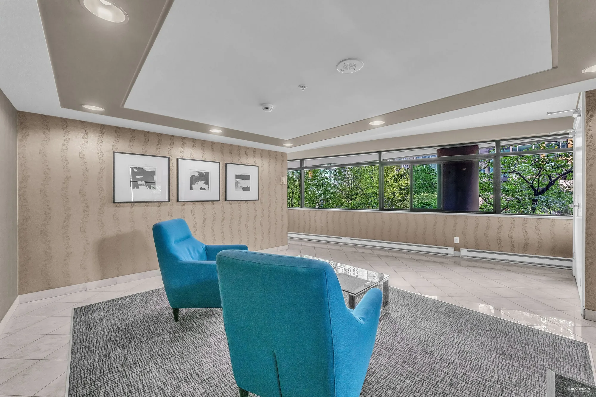 The lobby: two turquoise lounge chairs on a rug, framed prints, windows onto the trees