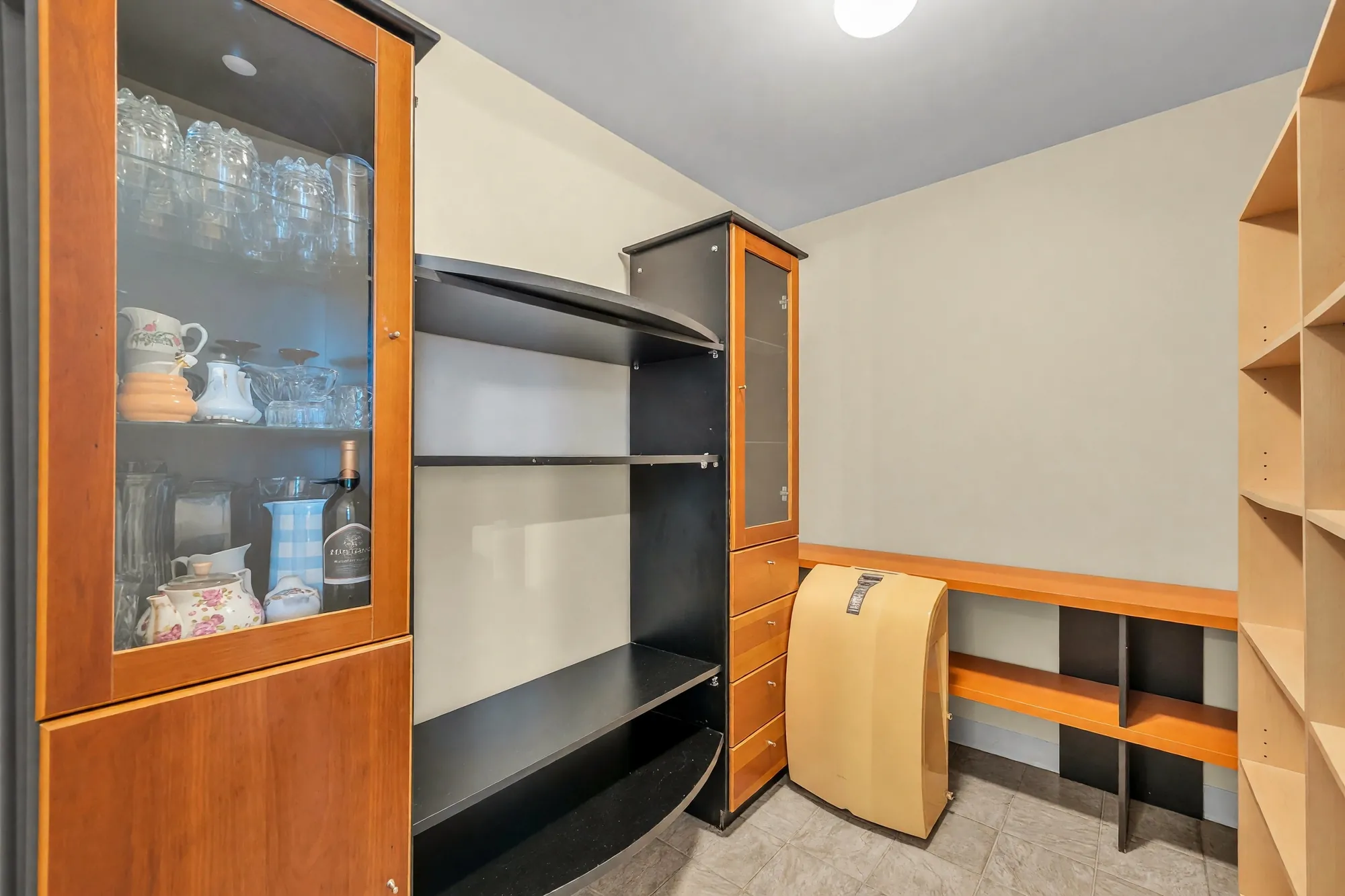 The office: a glass-fronted cabinet, a black and maple shelving unit, built-in shelves along the wall, a tiled floor