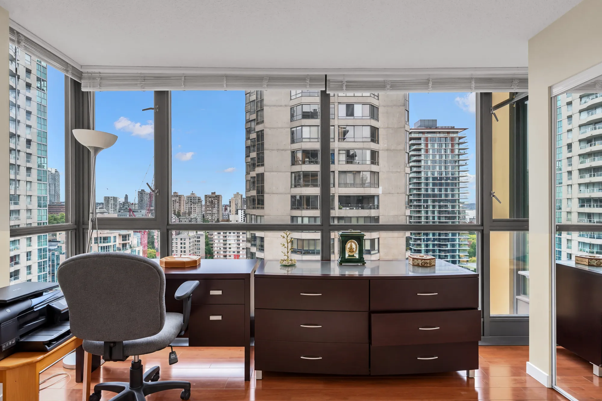 The desk end of the primary bedroom: a dark wood desk and drawers, an office chair, corner windows onto the towers